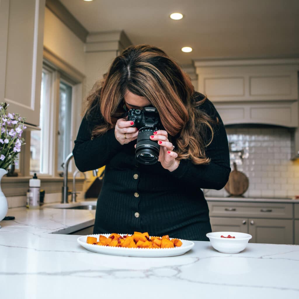 Amy Gorin holding a professional camera, photographing a plate of food.