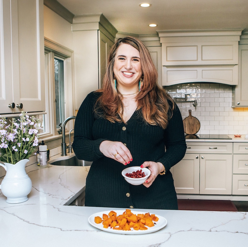 Amy Gorin standing in a kitchen holding a bowl of pomegranate arils.